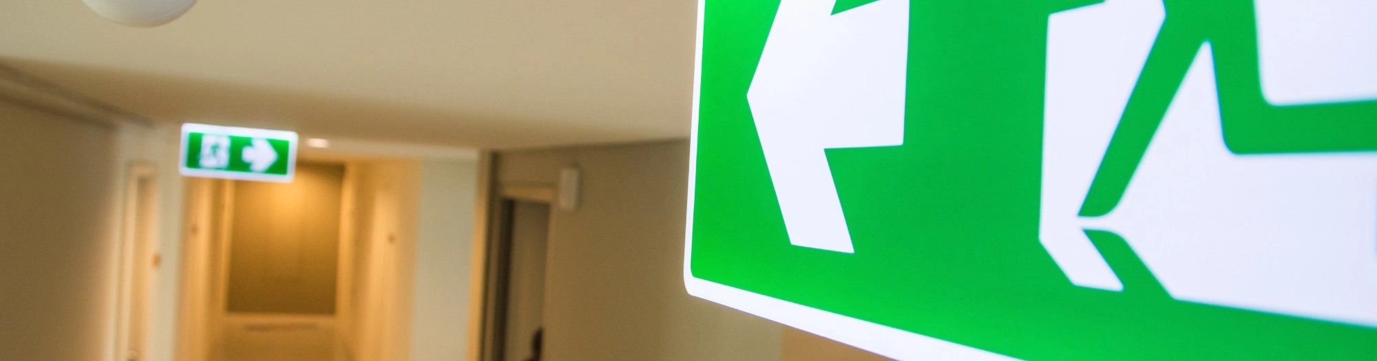 Green emergency exit signs in an office corridor