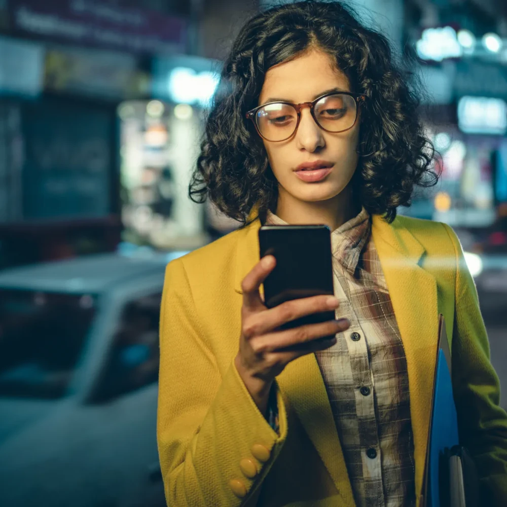 Business woman using phone on a busy road at night