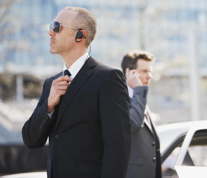 Male bodyguard talking into earpiece with male worker in the background